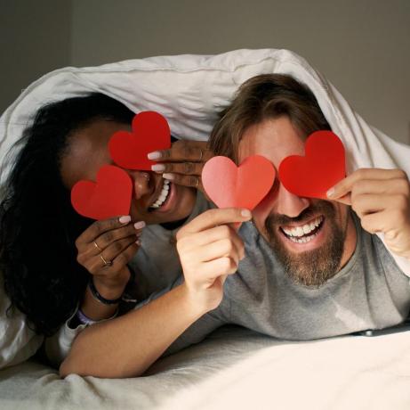 Pareja joven haciendo ojos de corazón en la cama juntos