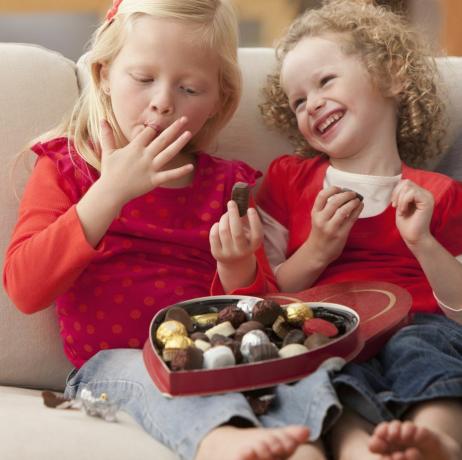 Dos niñas comiendo chocolates de una caja de dulces en forma de corazón