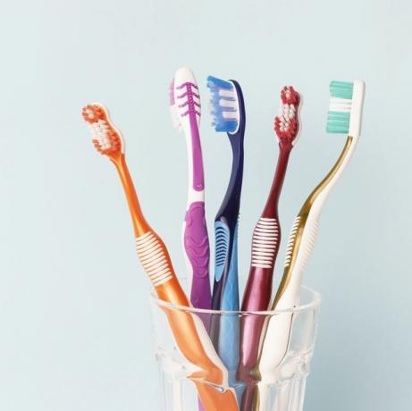 cepillos de dientes multicolores en un vaso de vidrio, fondo azul