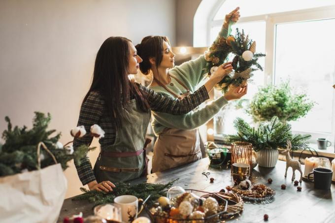 dos mujeres haciendo corona navideña con ramas de pino frescas y decoraciones festivas