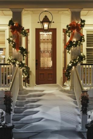 Invitando puerta de Navidad con nieve en las escaleras y barandilla del porche