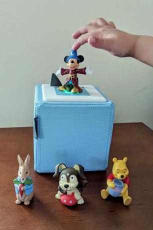 la mano de un niño alcanzando un juguete de mickey mouse un toniebox azul claro sobre una mesa de madera con un tonie de fantasía de mickey mouse