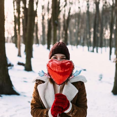 Joven mujer feliz en invierno en un día soleado sosteniendo un globo rojo en forma de corazón