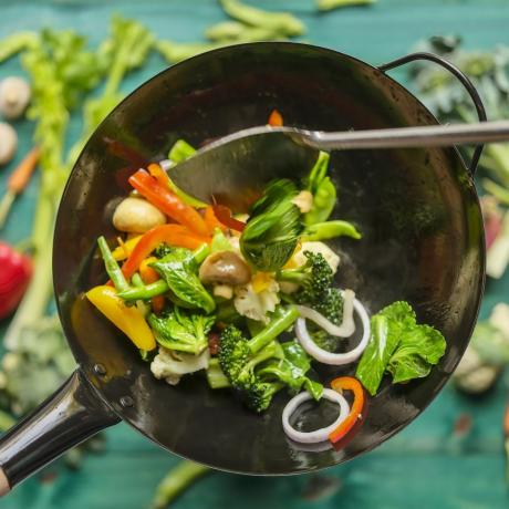 saltear y saltear una variedad de verduras frescas y coloridas del mercado en un wok humeante caliente con verduras sobre un fondo de mesa de madera de color turquesa debajo del wok